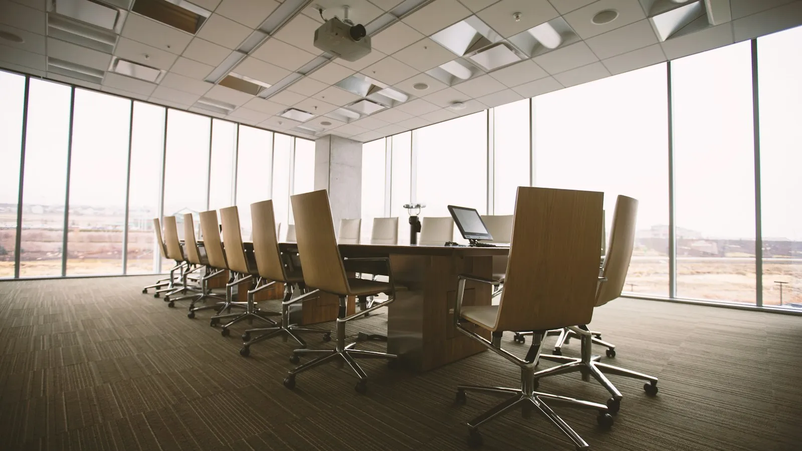 An empty boardroom with a long table and leather chairs before floor-to-ceiling windows.