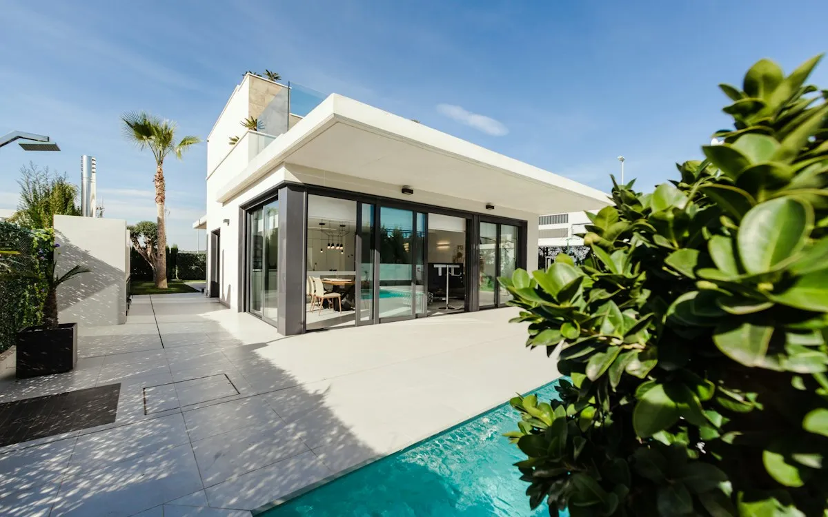 A modern white villa with floor-to-ceiling glass beside a pool.